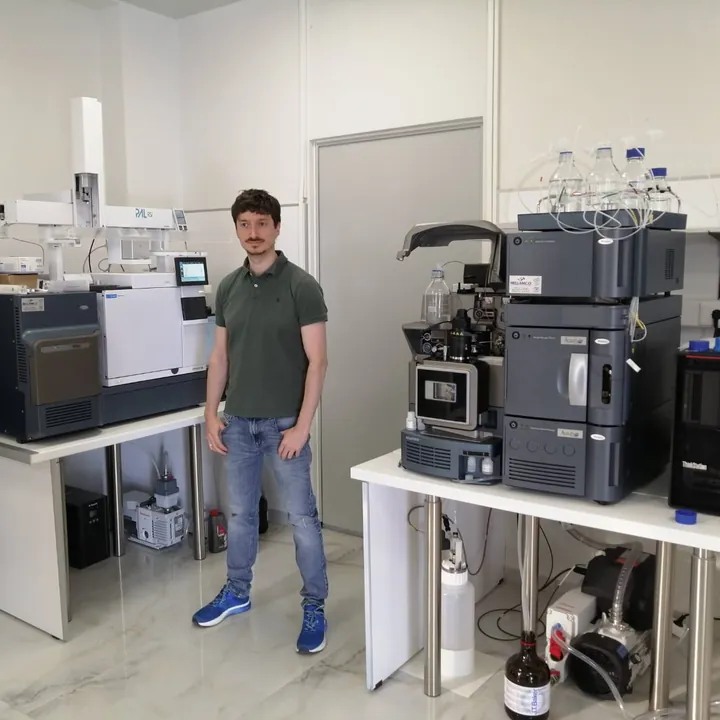 Guy Entract standing between a GC system and a Waters LC-MS system in a pharmaceutical laboratory